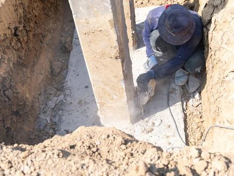 A construction worker kneeling in a pit, carefully using a power cutting to.. Foto stock