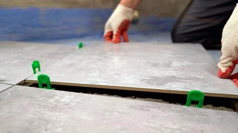 Construction worker laying ceramic tile on floor using tile leveling system Stock Photos