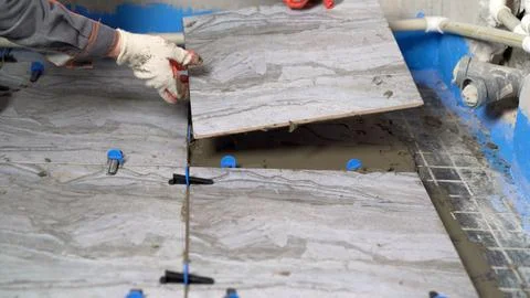 Construction worker laying down ceramic tile using tile leveling system. Stock Photos
