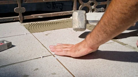 Construction worker laying floor tiles on outdoor terrace using spirit level Stock Footage 264094077