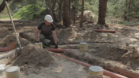Construction Worker Laying Underground Pipes in a Forested Area During Daylight Stock Footage 276430762