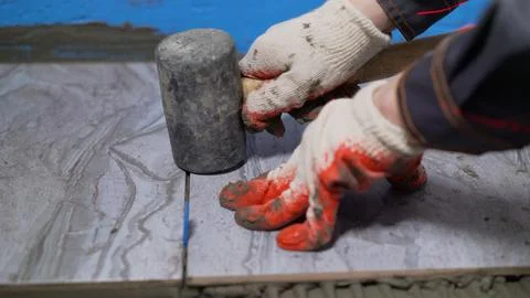 Construction worker leveling floor tiles with rubber mallet and leveling syst Stock Photos