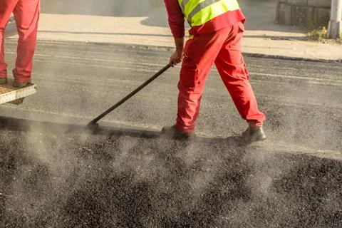 Construction worker leveling fresh asphalt pavement during road repair Stock Photos