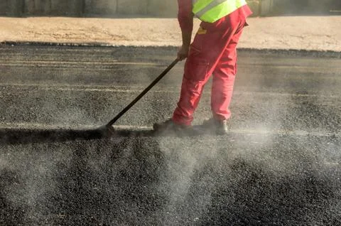Construction worker leveling fresh asphalt pavement during road repair Stock Photos