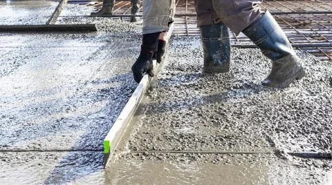Construction worker leveling a poured concrete floor in an industrial Photos