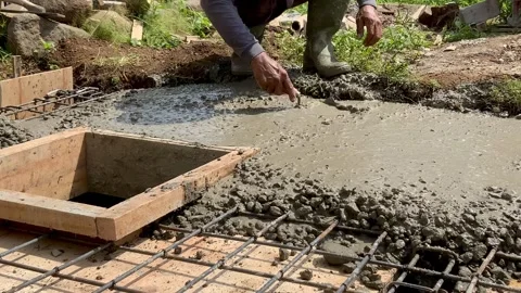Construction worker leveling wet concrete around a wooden formwork for a drainag Видео 334533645