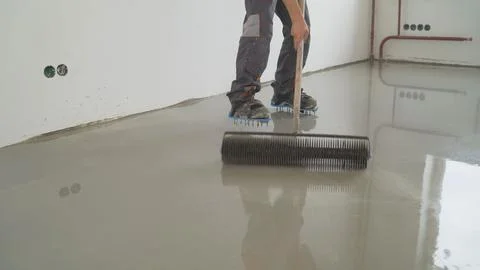 Construction worker levels wet concrete floor with spiked roller tool Stock-Fotos