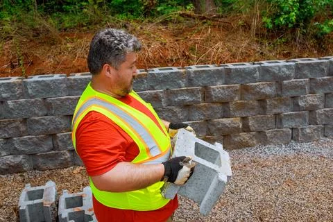 Construction worker lifted concrete block before mounting it on the retaining Stock Photos