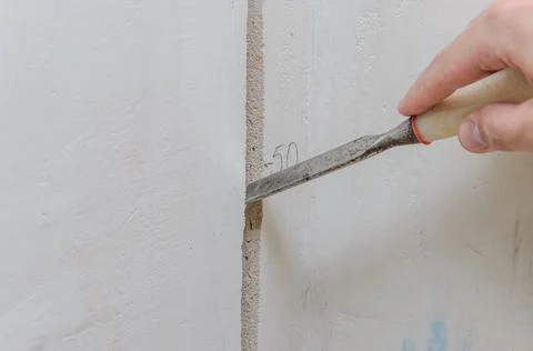 Construction worker makes a hole in the wall for electrical wiring with a chisel Stock Photos