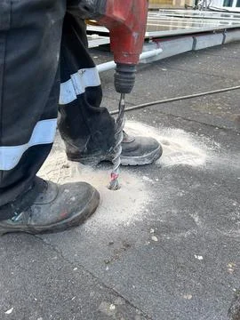 Construction worker making a hole in the concrete floor with a drill. Stock Photos