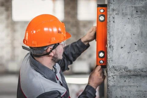 Construction worker man in a hard hat and overalls checks the vertical level of Stock Photos