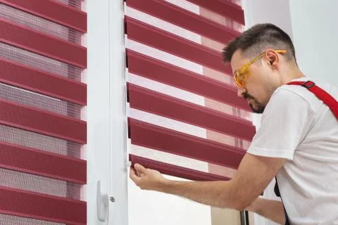 Construction worker man in a uniform install blinds on plastic white upvc Stock Photos