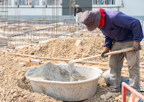 Construction worker manually mixing cement and sand in a plastic tub on a b.. Foto stock