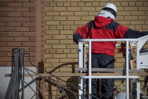 Construction worker mason in cherry picker restoring brick wall Stock-Fotos