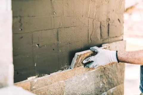 Construction worker mason closely placing stone tile on vertical wall Stock Photos