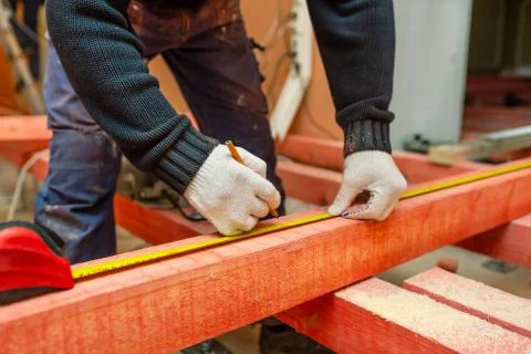 Construction worker measures distance before to saw the woodeb block in Stock Photos