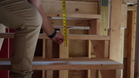 Construction worker measures with measurement tape the size of wooden stairs at Stock Footage 317062479