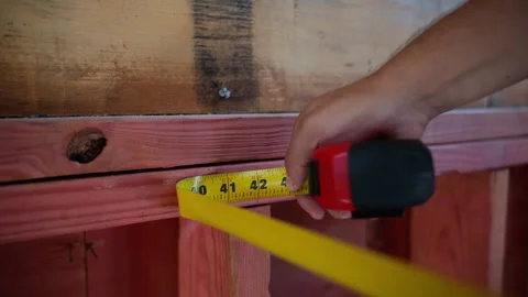 Construction worker measures with measurement tape the size of wooden plank at 库存影片 317062706