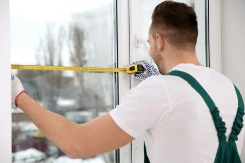 Construction worker measuring plastic window indoors. Professional installati Stock Photos