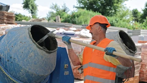 Construction Worker Mixing Cement in Drum Mixer, Wearing Orange Safety Vest and Stock Footage 312443282