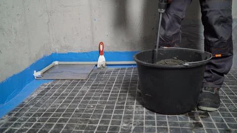 Construction worker mixing mortar in a bucket on a tiled floor during renov.. Stock-Fotos