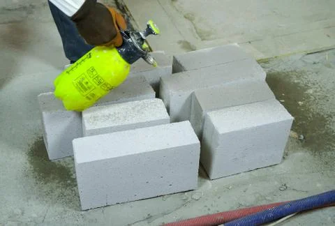 Construction worker moisturing aerated concrete blocks with water sprayer Stock Photos