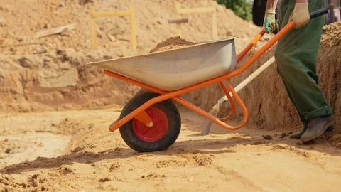 Construction worker moving sand with wheelbarrow at site Stock Photos
