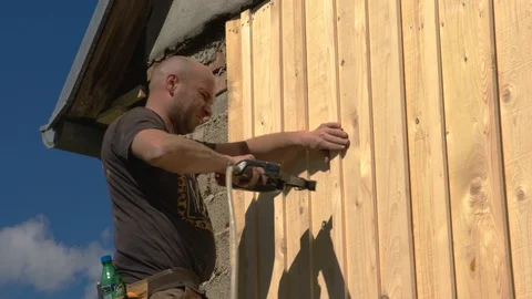 Construction worker nails boards with nailing machine Stock Footage 99891219