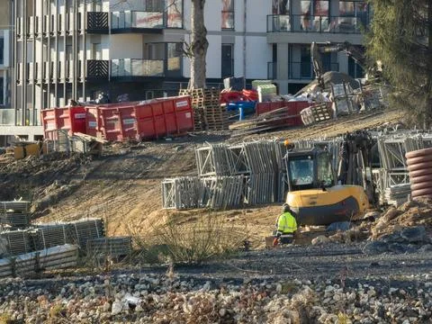A construction worker operates an excavator near steel scaffolding and Stock Photos