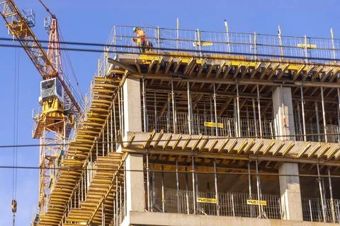 A construction worker operates on an unfinished high-rise building with a tall Stock Photos