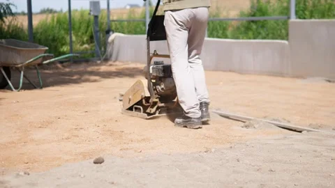 Construction worker operating plate compactor on dusty outdoor building site Stock Footage 344873602