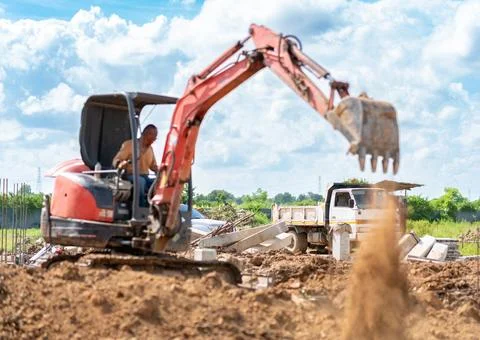 Construction worker operating a small crawler excavator bucket to scoop soi.. Stock Photos