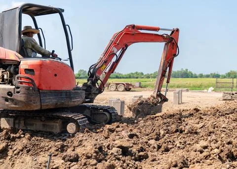 A construction worker operating a small orange excavator to move earth on a.. Foto stock