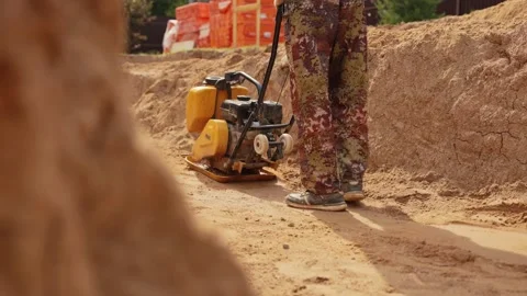 Construction worker operating a vibratory plate compactor on sand Stock Footage 341294835