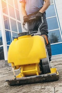 Construction Worker Operating a Yellow Plate Compactor on Site Foto stock