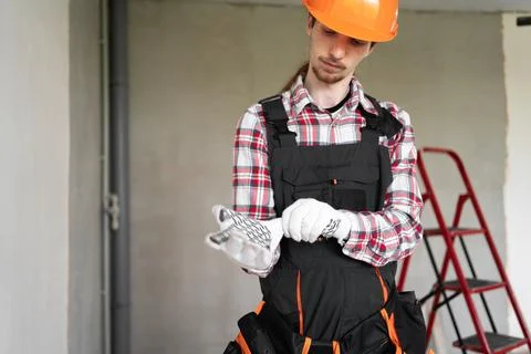Construction worker or young builder putting gloves before work standing in h Stock Photos