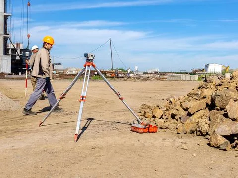 A construction worker in an orange hardhat walks past an optical level at a Stock-Fotos