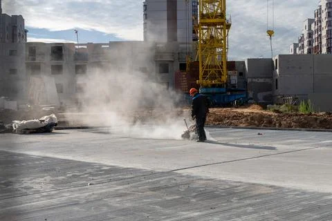 Construction worker in orange helmet cutting concrete slab with dust cloud Stock Photos
