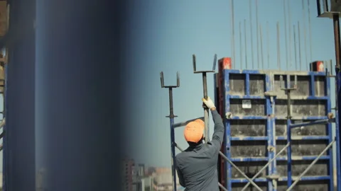 Construction worker in orange helmet installing metal support at building site Stock Footage 318780027
