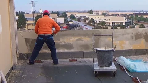 Construction worker in an orange jacket and blue pants is plastering a wall o Vídeo Stock 300497226
