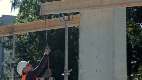 Construction worker in orange vest and white helmet pulling rope at concrete Stock Footage 317882546