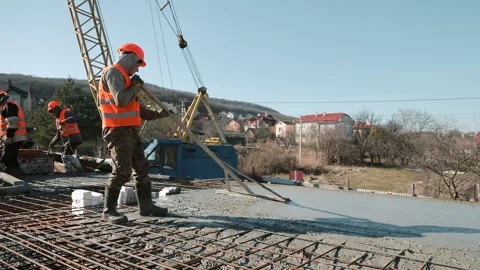 Construction worker in orange vest levels wet concrete slab with long wooden Stock Footage 306405544