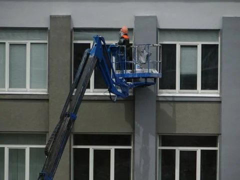 Construction worker painting building facade using aerial lift Stock Photos