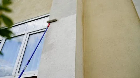 Construction worker is painting a building using a paint roller on a telesc.. Stock Photos
