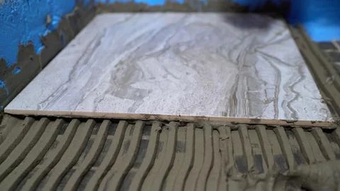 Construction worker placing ceramic tile on wet cement mortar using tile le.. Stock Photos