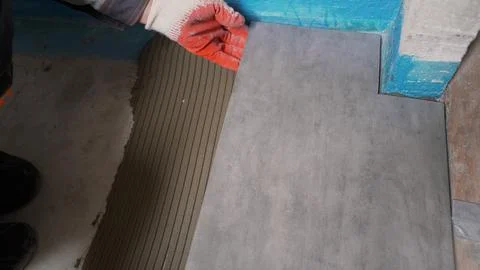 Construction worker placing large grey tile on floor with cement glue Stock Photos