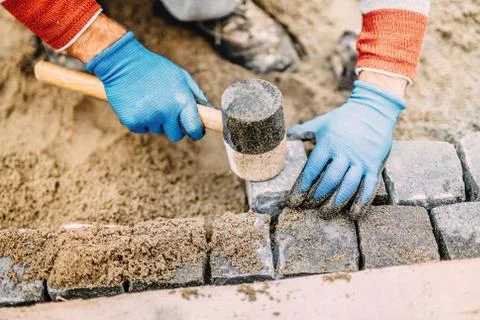 Construction worker placing stone tiles, cobblestone blocks in sand Stock Photos