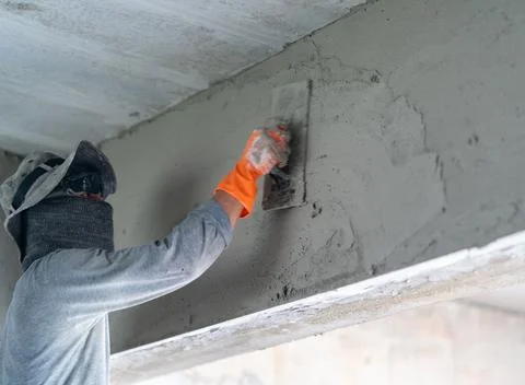 Construction worker plastering a concrete wall surface during house renovatio Stock Photos