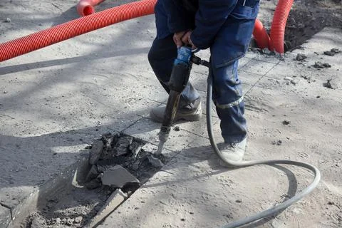 A construction worker with a pneumatic hammer breaks the asphalt. Stock Photos