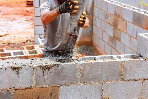 Construction worker pouring concrete into block walls at building site in warm Fotos de archivo